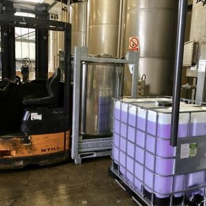 Photograph of industrial chemical vats with a forklift and a 1000 litre IBC container labelled Pearl Waterless Advanced Ultra Nano Concentrate product on a clean concrete factory floor.